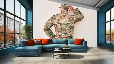 Young caucasian man wearing camouflage army uniform backwards thinking about doubt with hand on head Wall mural