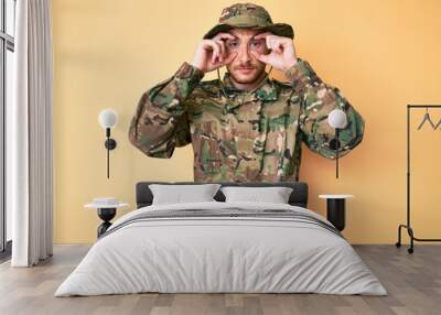 Young caucasian man wearing camouflage army uniform trying to open eyes with fingers, sleepy and tired for morning fatigue Wall mural