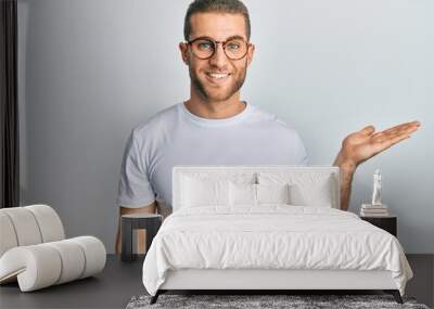 Young caucasian man wearing casual clothes and glasses smiling cheerful presenting and pointing with palm of hand looking at the camera. Wall mural