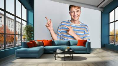 Young caucasian man wearing casual striped t shirt smiling and looking at the camera pointing with two hands and fingers to the side. Wall mural