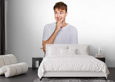 Young caucasian man wearing casual white t shirt with hand on chin thinking about question, pensive expression. smiling with thoughtful face. doubt concept. Wall mural