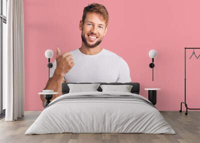 Young caucasian man wearing casual white tshirt smiling with happy face looking and pointing to the side with thumb up. Wall mural