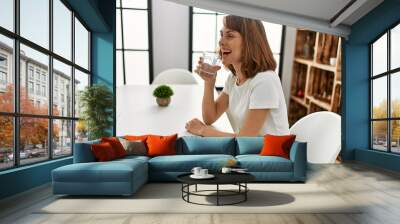 Young caucasian woman drinking water sitting on table at home Wall mural