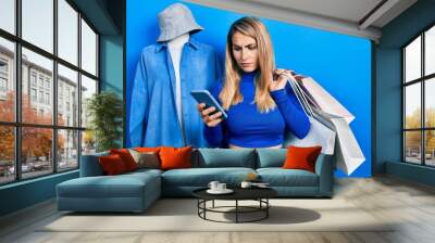 Young caucasian woman holding shopping bags and smartphone skeptic and nervous, frowning upset because of problem. negative person. Wall mural