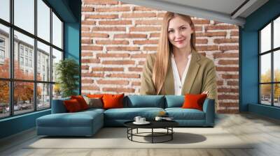 Young caucasian woman standing over bricks wall background happy face smiling with crossed arms looking at the camera. positive person. Wall mural