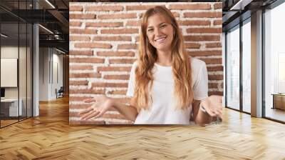 Young caucasian woman standing over bricks wall smiling cheerful with open arms as friendly welcome, positive and confident greetings Wall mural