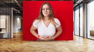 Young caucasian woman standing over red background with hand on stomach because indigestion, painful illness feeling unwell. ache concept. Wall mural