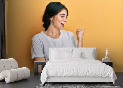 Young caucasian woman wearing casual white t shirt smiling with happy face looking and pointing to the side with thumb up. Wall mural