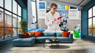 Young caucasian woman wearing scientist uniform using touchpad working at laboratory Wall mural