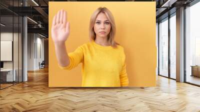 Young caucasian woman wearing yellow sweater doing stop sing with palm of the hand. warning expression with negative and serious gesture on the face. Wall mural