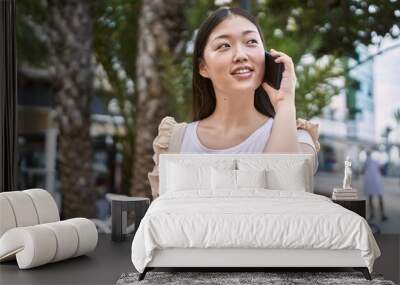 Young chinese girl smiling happy talking on the smartphone at the city. Wall mural