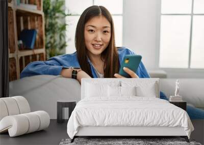 Young chinese girl using smartphone sitting on the sofa at home. Wall mural