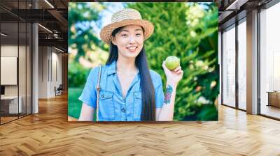 Young chinese tourist woman eating green apple at the park. Wall mural