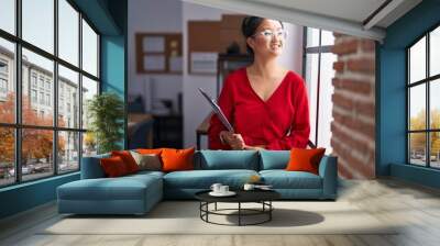 Young chinese woman business worker smiling confident holding clipboard at office Wall mural