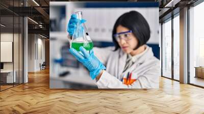 Young chinese woman scientist holding measuring liquid at laboratory Wall mural