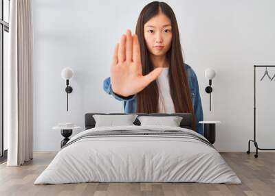 Young chinese woman wearing denim shirt standing over isolated white background doing stop sing with palm of the hand. Warning expression with negative and serious gesture on the face. Wall mural