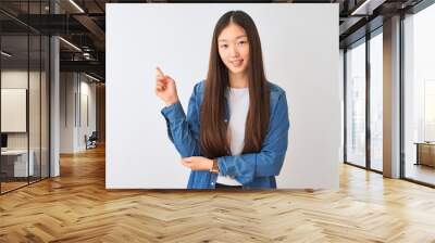 Young chinese woman wearing denim shirt standing over isolated white background with a big smile on face, pointing with hand and finger to the side looking at the camera. Wall mural