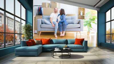 Young couple in love relaxing and hugging sitting on the sofa at new home, smiling very happy for moving to a new apartment Wall mural