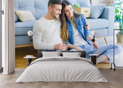 Young couple sitting on the floor of new home using computer laptop and smiling happy for moving to a new home Wall mural