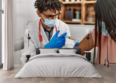 Young doctor man injecting covid-19 coronavirus vaccine for woman sitting on the sofa at the clinic. Wall mural