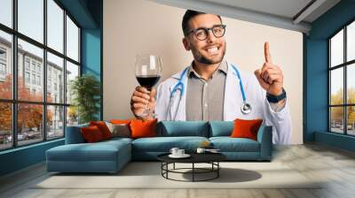 Young doctor man wearing stethoscope drinking a glass of fresh wine over isolated background surprised with an idea or question pointing finger with happy face, number one Wall mural