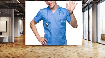 Young doctor wearing medical uniform over isolated background Waiving saying hello happy and smiling, friendly welcome gesture Wall mural