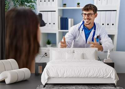 Young doctor with client at medical clinic pointing fingers to camera with happy and funny face. good energy and vibes. Wall mural