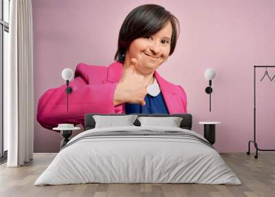 Young down syndrome business woman over pink background doing happy thumbs up gesture with hand. Approving expression looking at the camera showing success. Wall mural