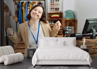 Young down syndrome woman working as manager at retail boutique very happy and excited doing winner gesture with arms raised, smiling and screaming for success. celebration concept. Wall mural