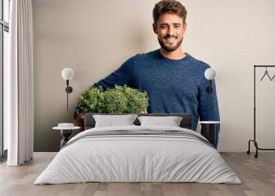 Young gardener man with beard holding box with plants standing over white background with a happy face standing and smiling with a confident smile showing teeth Wall mural