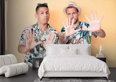 Young gay couple of two men wearing summer hat and hawaiian shirt moving away hands palms showing refusal and denial with afraid and disgusting expression. stop and forbidden. Wall mural