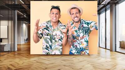 Young gay couple of two men wearing summer hat and hawaiian shirt shouting frustrated with rage, hands trying to strangle, yelling mad Wall mural