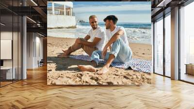 Young gay couple smiling happy sitting at the beach. Wall mural