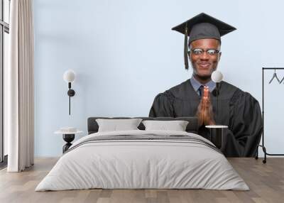 Young graduated african american man over isolated background praying with hands together asking for forgiveness smiling confident. Wall mural