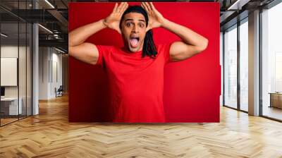 Young handsome african american afro man with dreadlocks wearing red casual t-shirt Smiling cheerful playing peek a boo with hands showing face. Surprised and exited Wall mural