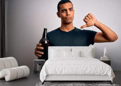 Young handsome african american man drinking bottle of beer over white background with angry face, negative sign showing dislike with thumbs down, rejection concept Wall mural