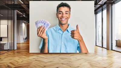 Young handsome african american man holding 20 swedish krona banknotes smiling happy and positive, thumb up doing excellent and approval sign Wall mural