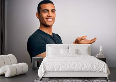 Young handsome african american man wearing casual t-shirt standing over white background pointing aside with hands open palms showing copy space, presenting advertisement smiling excited happy Wall mural