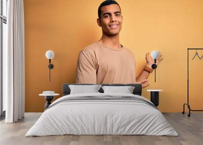 Young handsome african american man wearing casual t-shirt standing over yellow background Inviting to enter smiling natural with open hand Wall mural