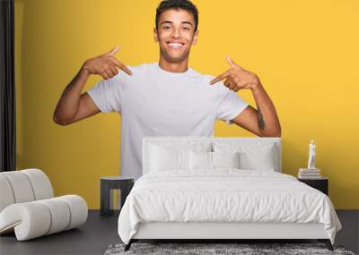 Young handsome african american man wearing casual white tshirt looking confident with smile on face, pointing oneself with fingers proud and happy. Wall mural