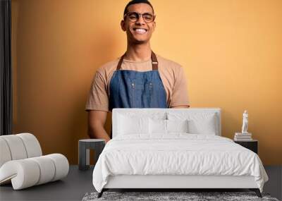 Young handsome african american shopkeeper man wearing apron over yellow background with a happy and cool smile on face. Lucky person. Wall mural