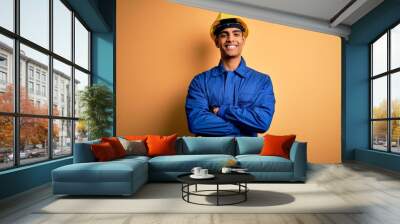 Young handsome african american worker man wearing blue uniform and security helmet happy face smiling with crossed arms looking at the camera. Positive person. Wall mural