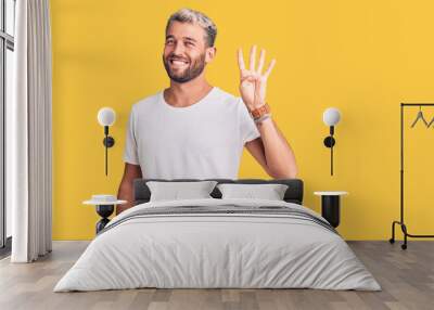 Young handsome blond man wearing casual t-shirt showing and pointing up with fingers number four while smiling confident and happy. Wall mural