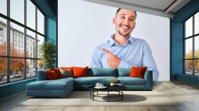 Young handsome business man standing over isolated background with a big smile on face, pointing with hand and finger to the side looking at the camera. Wall mural