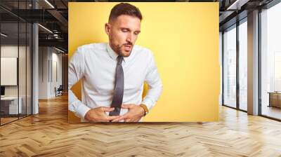 Young handsome business man wearing elegant white shirt over yellow isolated background with hand on stomach because indigestion, painful illness feeling unwell. Ache concept. Wall mural