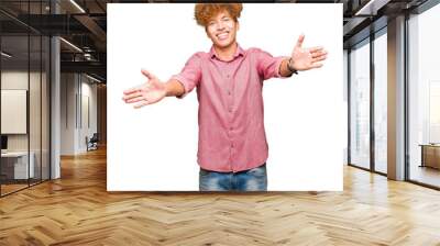 Young handsome business man with afro hair looking at the camera smiling with open arms for hug. Cheerful expression embracing happiness. Wall mural