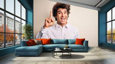 Young handsome businessman wearing elegant shirt standing over isolated white background pointing finger up with successful idea. Exited and happy. Number one. Wall mural