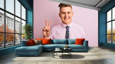 Young handsome businessman wearing shirt and tie standing over isolated pink background showing and pointing up with fingers number two while smiling confident and happy. Wall mural