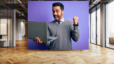 Young handsome businessman with beard working using laptop over purple background screaming proud and celebrating victory and success very excited, cheering emotion Wall mural