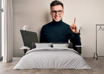 Young handsome caucasian business man wearing glasses using computer laptop surprised with an idea or question pointing finger with happy face, number one Wall mural